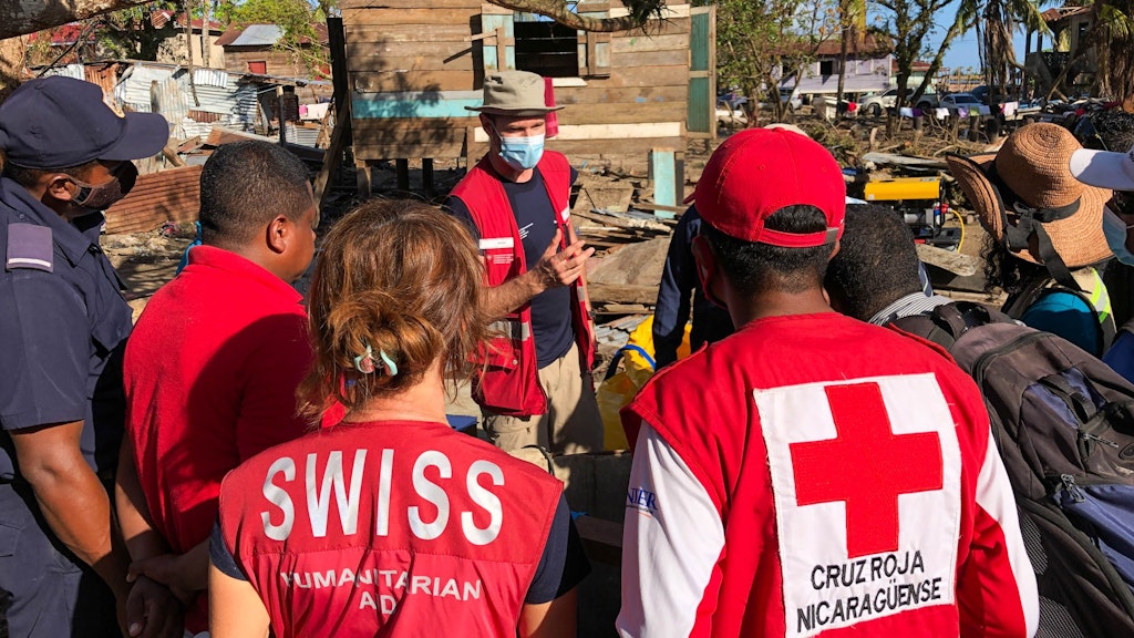 SDC personnel and local reconstruction personnel in Discussion. In the background a damaged wooden house.