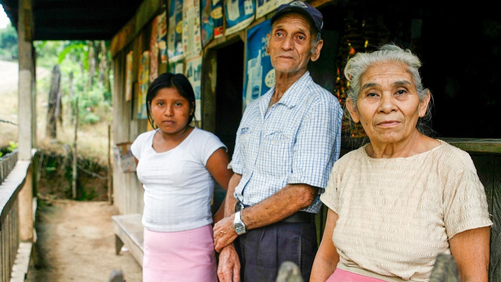 Una pareja de ancianos posa frente a su tienda con su nieta.